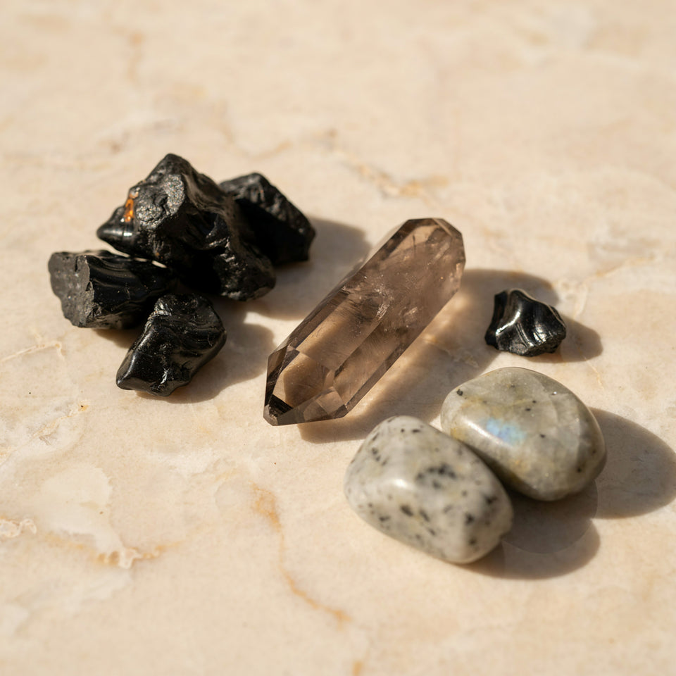 Raw rough black obsidian, smoky quartz and labradorite stones on a cream stone surface