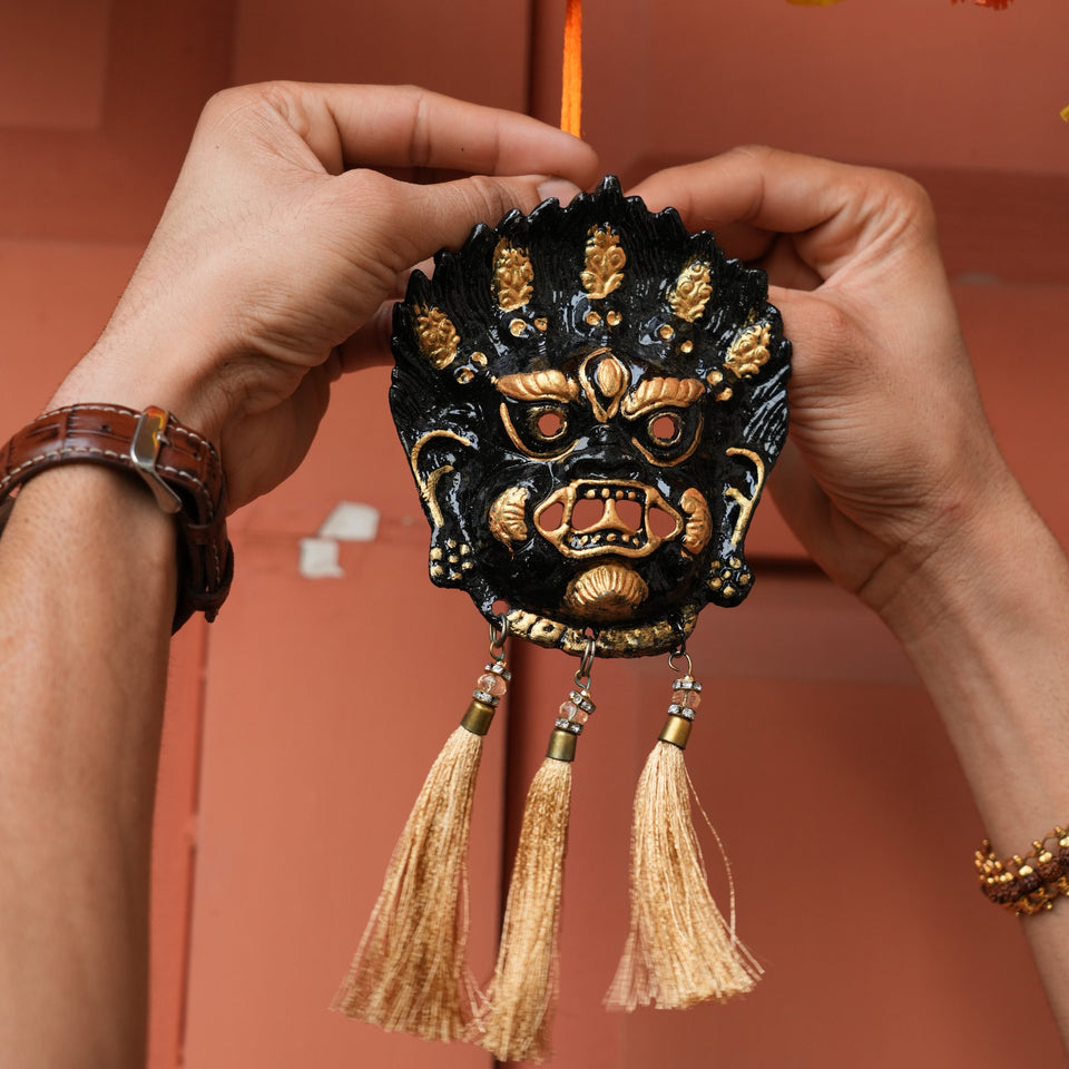 Black Kirtimukh wall hanging with three golden tassels held in two hands