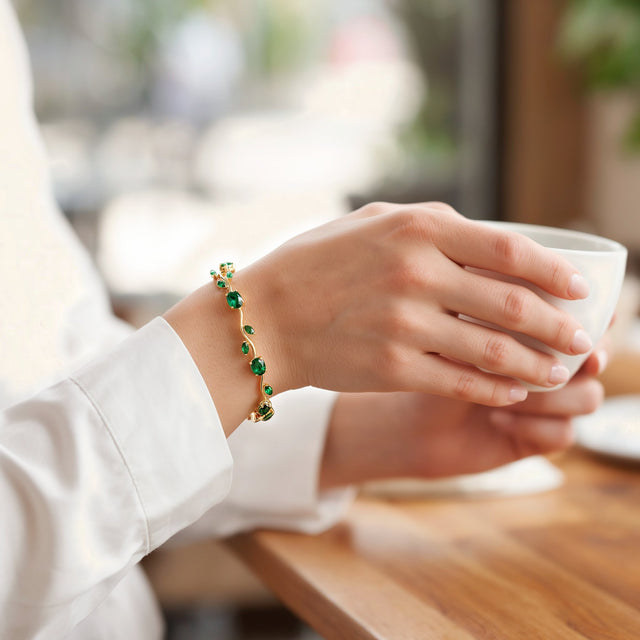A woman's hand around a coffee cup at a cafe table, wearing the green tulip bracelet