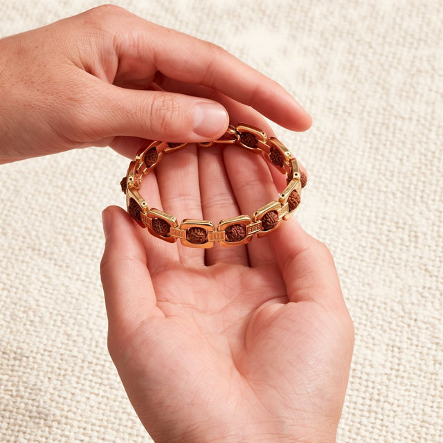 A hand holding a gold link Rudraksha bracelet open above the other open hand