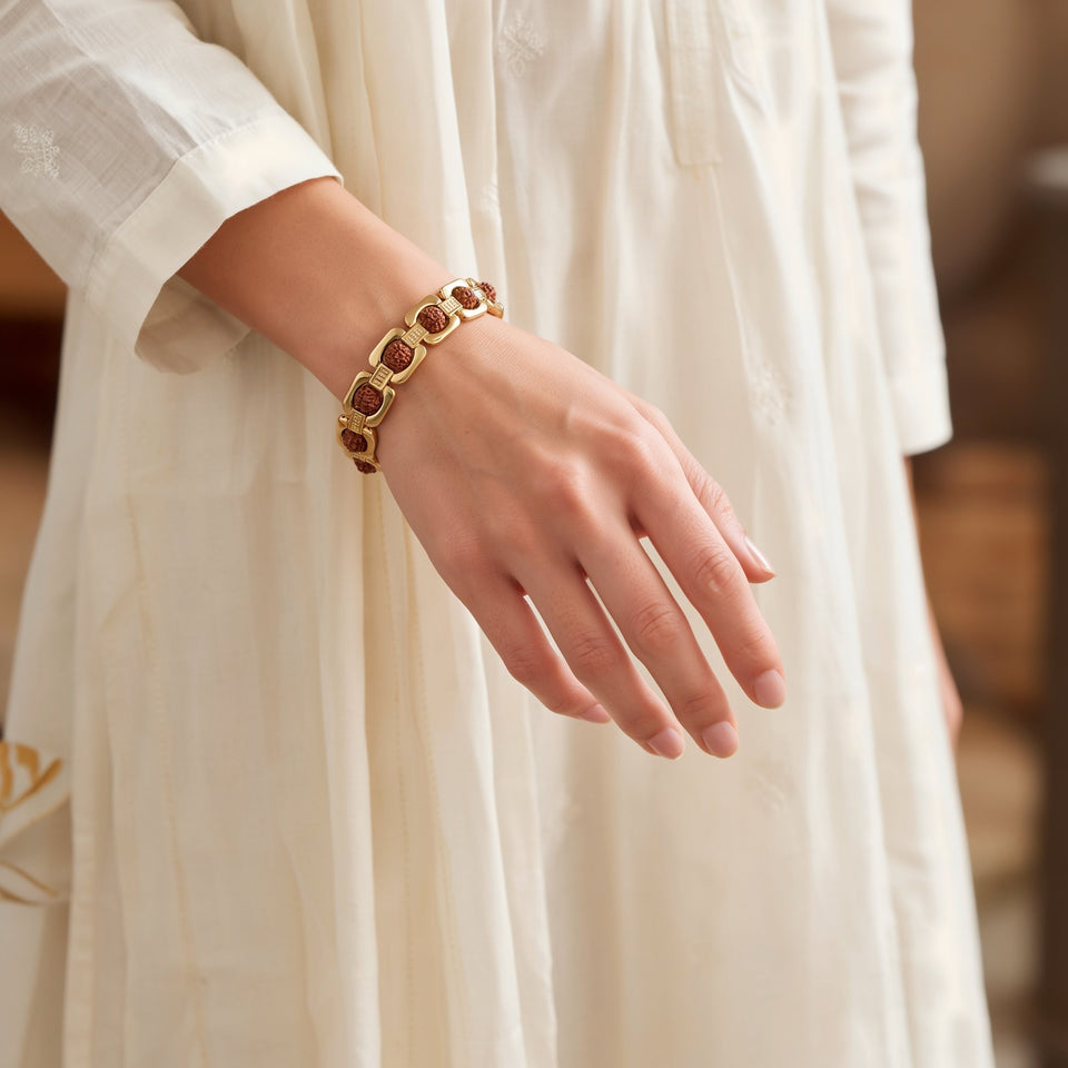 Woman's wrist wearing a gold plated rudraksha bracelet with an ivory kurta sleeve