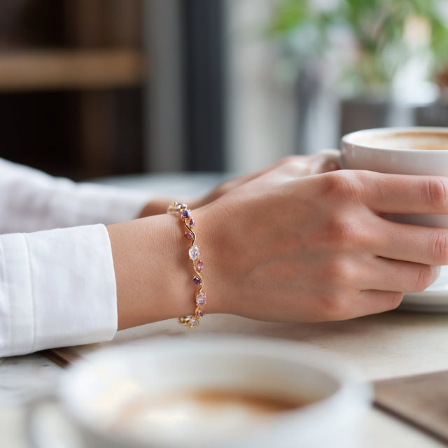 A woman's hand around a coffee cup on a cafe table, wearing the pink and purple tulip bracelet