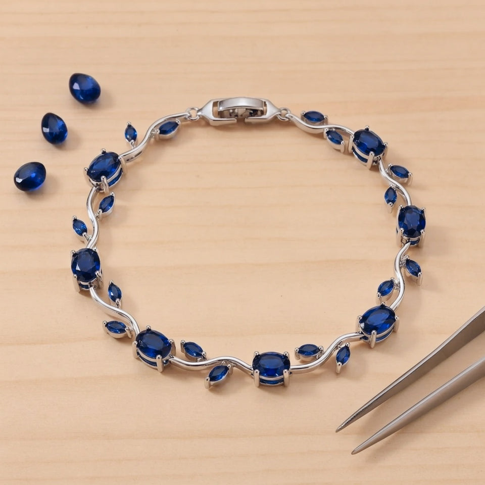 Blue tulip bracelet laid flat on a pale craft bench with loose deep blue stones and tweezers