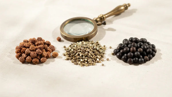 Piles of rudraksha, pyrite and karungali beads with a magnifying glass on cream cloth