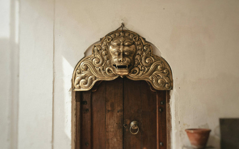 Kirtimukh brass wall hanging above a wooden main door of an Indian home