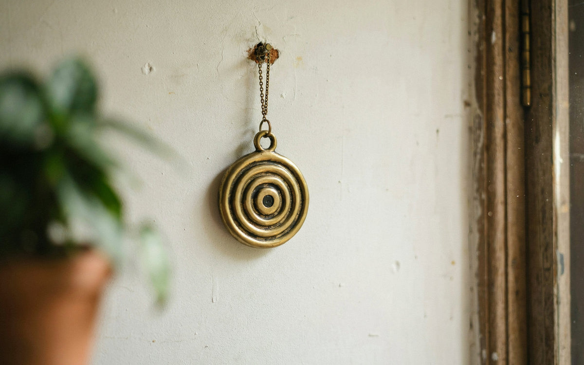 Brass nazar battu hung on a house wall near a doorway with a blurred potted plant