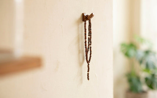 A tulsi bead mala hanging from a small wooden hook in front