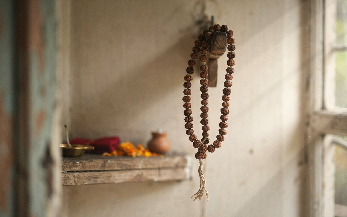 Rudraksha mala hung on a wooden peg near a small home mandir