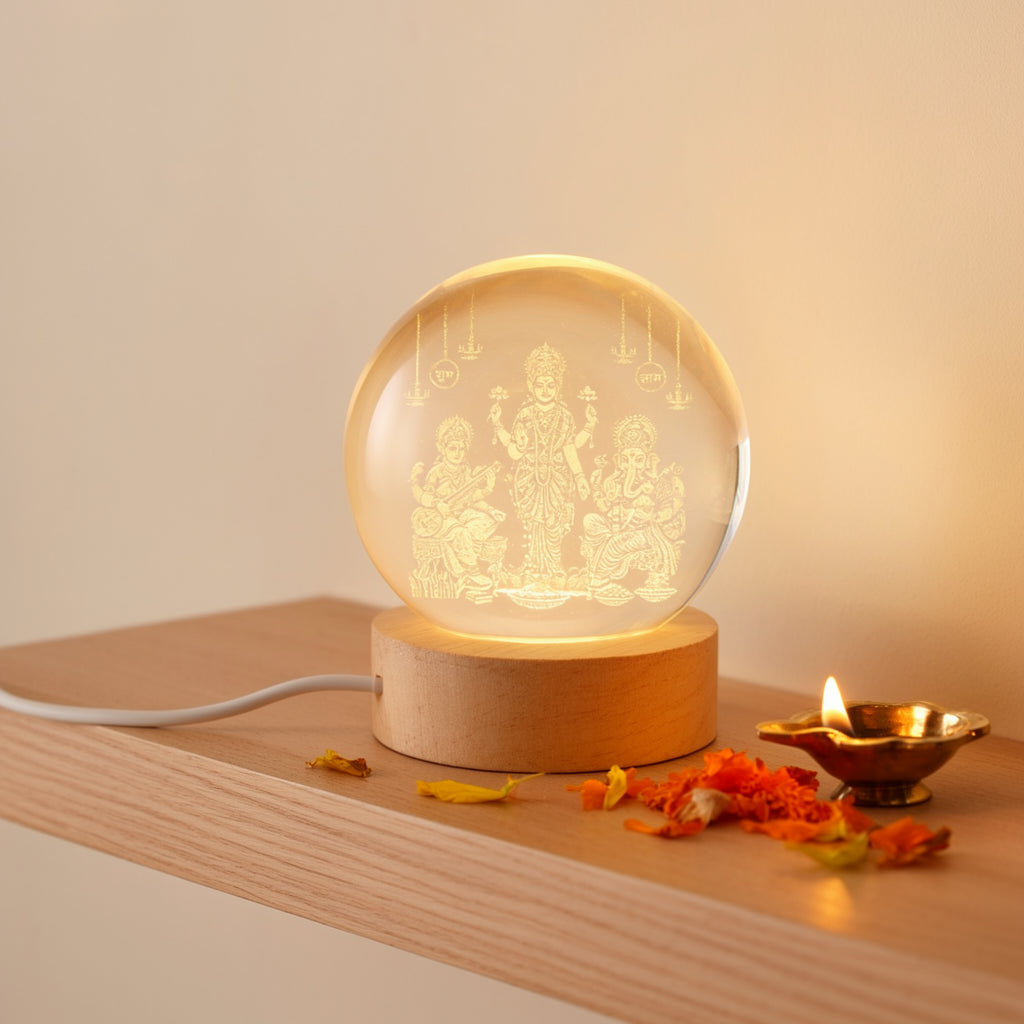 Lakshmi Saraswati Ganesh Ji 3D crystal ball lamp on a wooden wall shelf with a brass diya and marigold petals