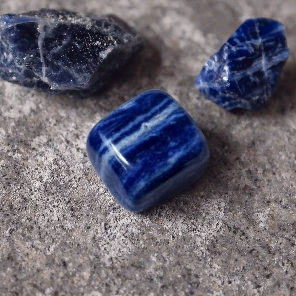 Sodalite tumble beside two raw blue sodalite rough chunks with white veining