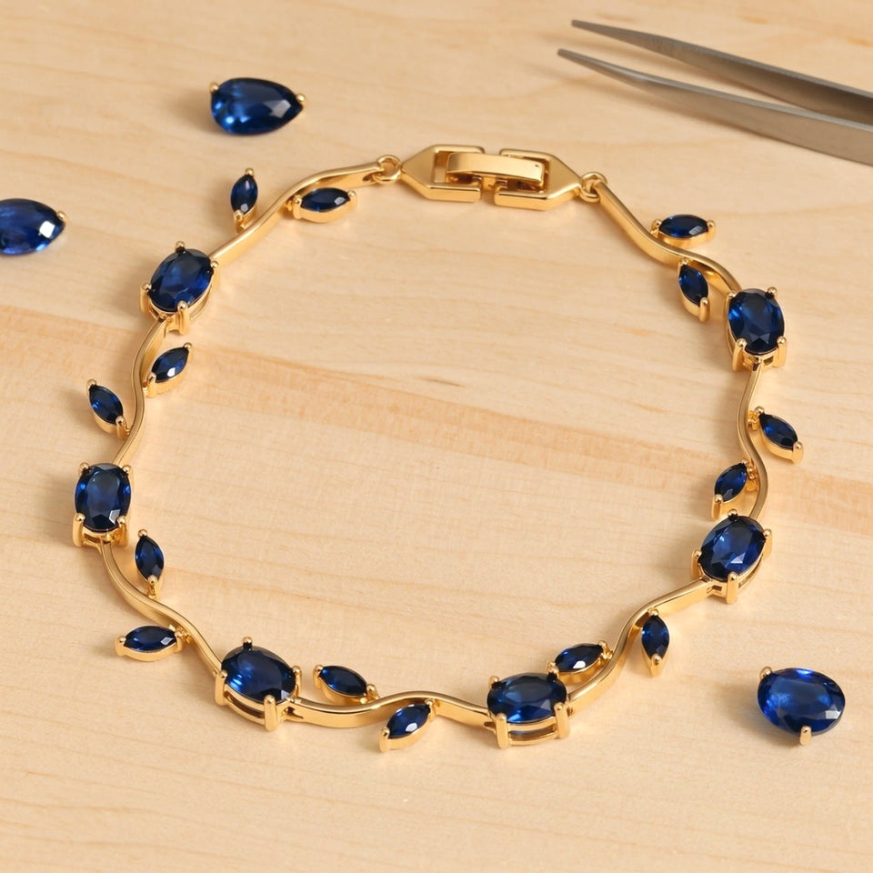 Gold tone tulip bracelet with blue stones laid flat on a pale craft bench with loose blue stones and tweezers