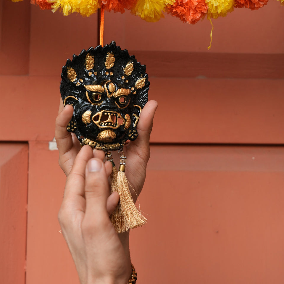 Black Kirtimukh wall hanging with golden tassels held up in one hand, close view of the face and tassels