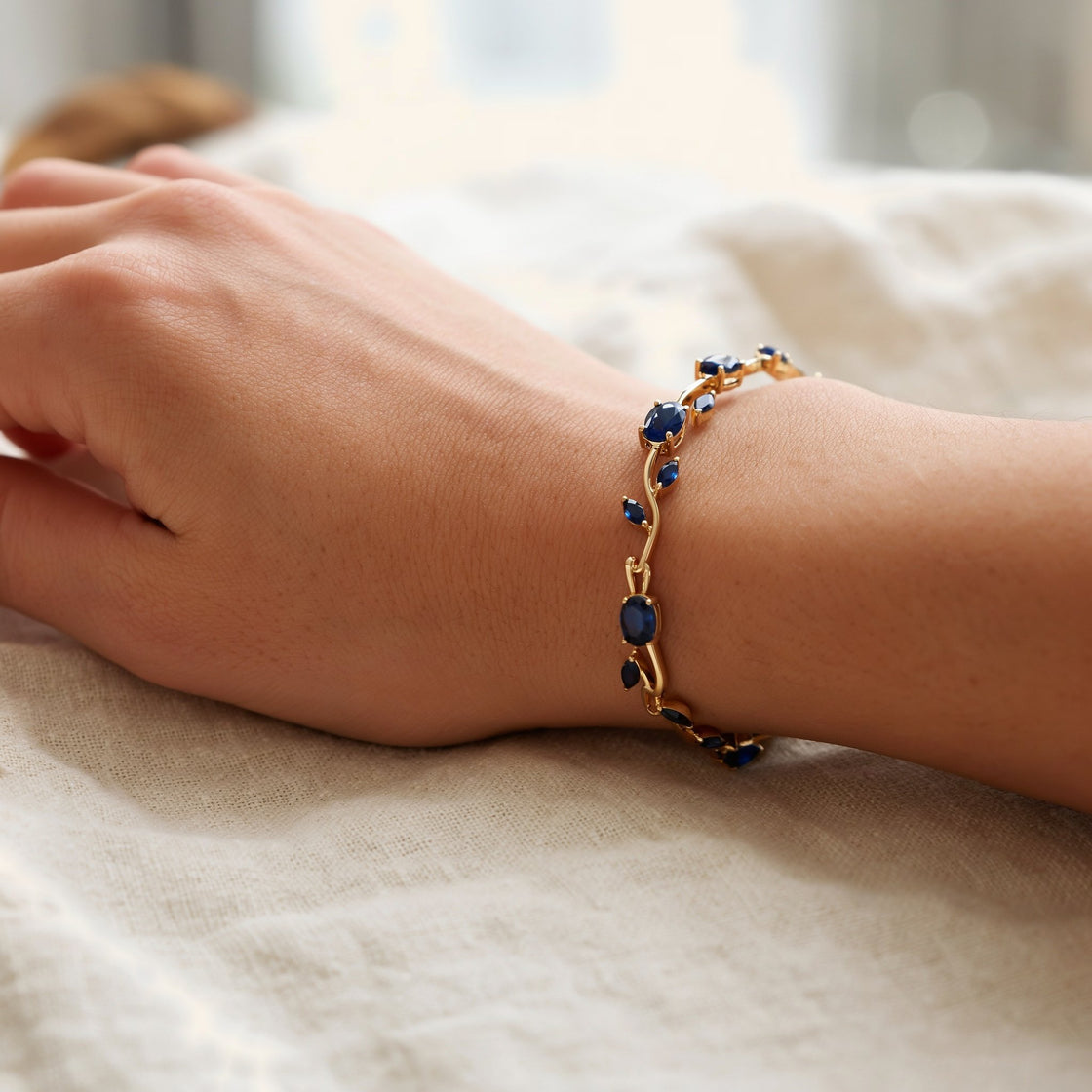 A woman's wrist resting on cream linen, wearing the blue tulip gold tone bracelet
