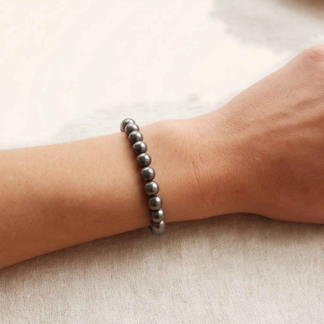 Woman's wrist wearing a stretch bracelet of round natural pyrite beads on cream linen
