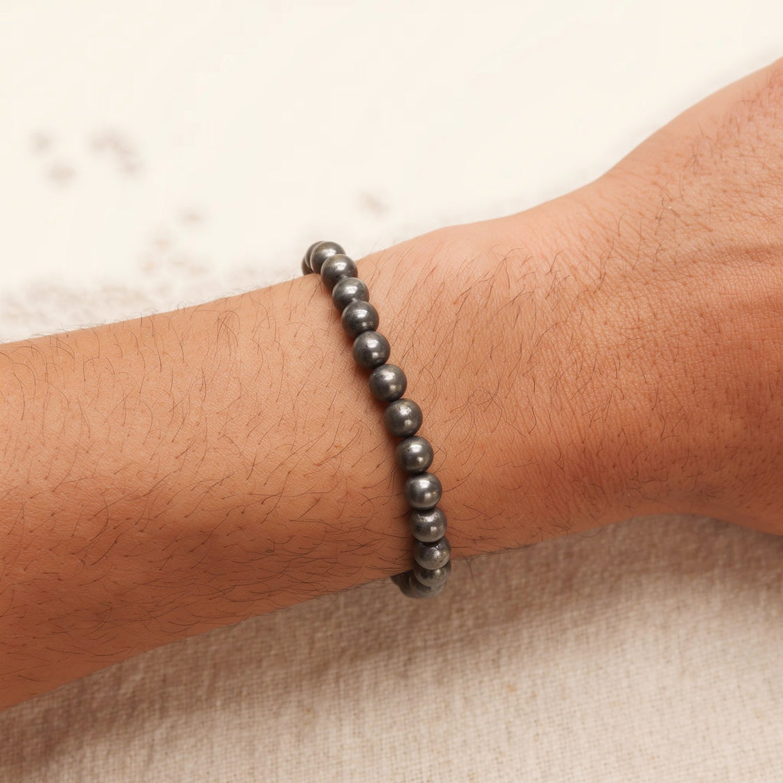 Man's wrist wearing a stretch bracelet of round natural pyrite beads on cream linen