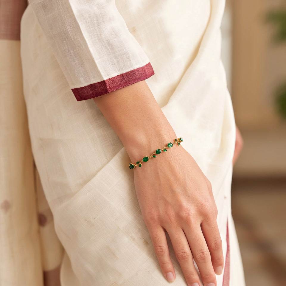 A woman's wrist in an ivory saree sleeve with a maroon border, wearing the green tulip bracelet