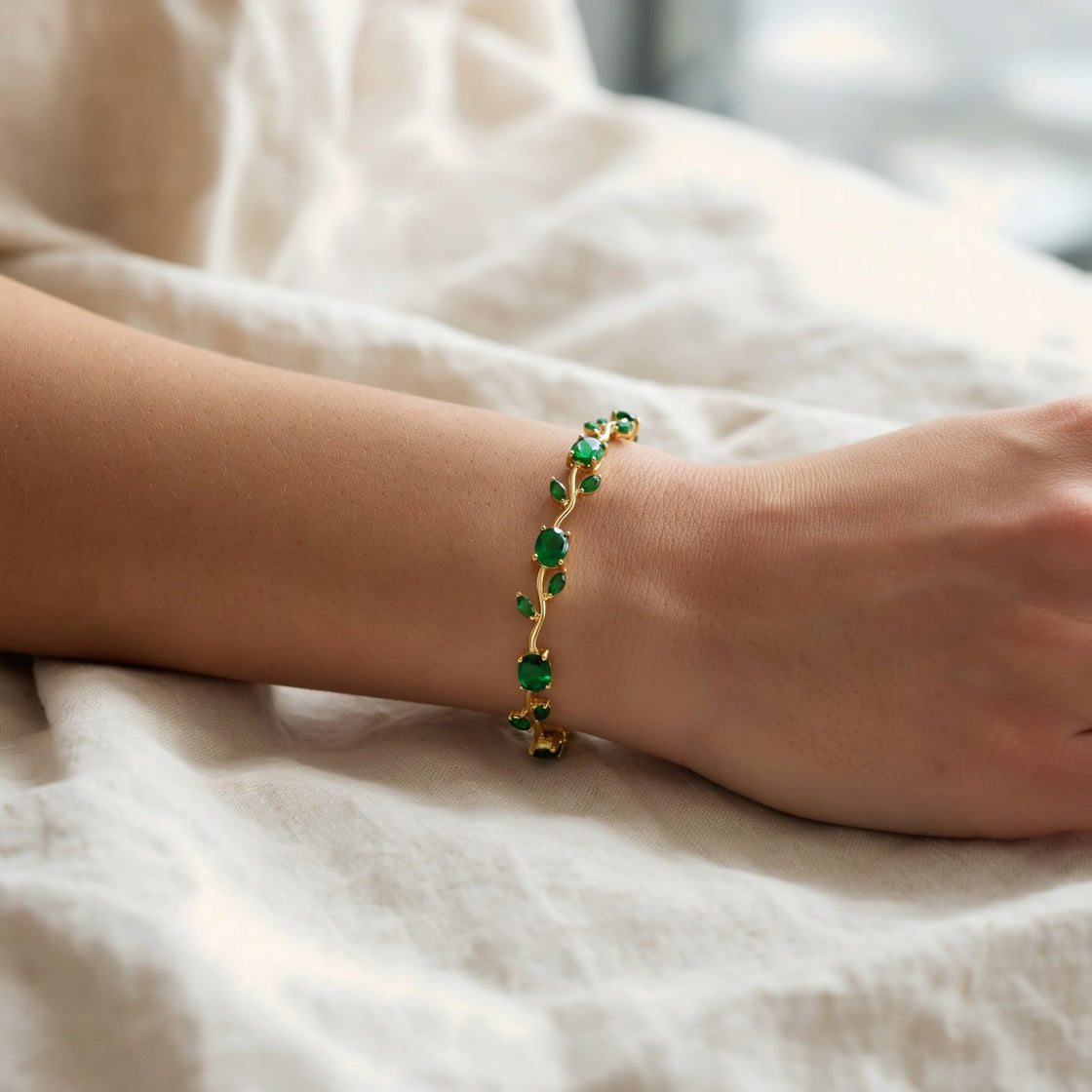 A woman's wrist resting on cream linen, wearing the green tulip bracelet