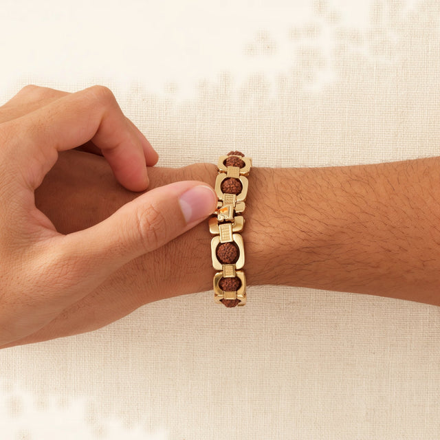 Thumb pressing the clasp of a gold link Rudraksha bracelet closed on a man's wrist