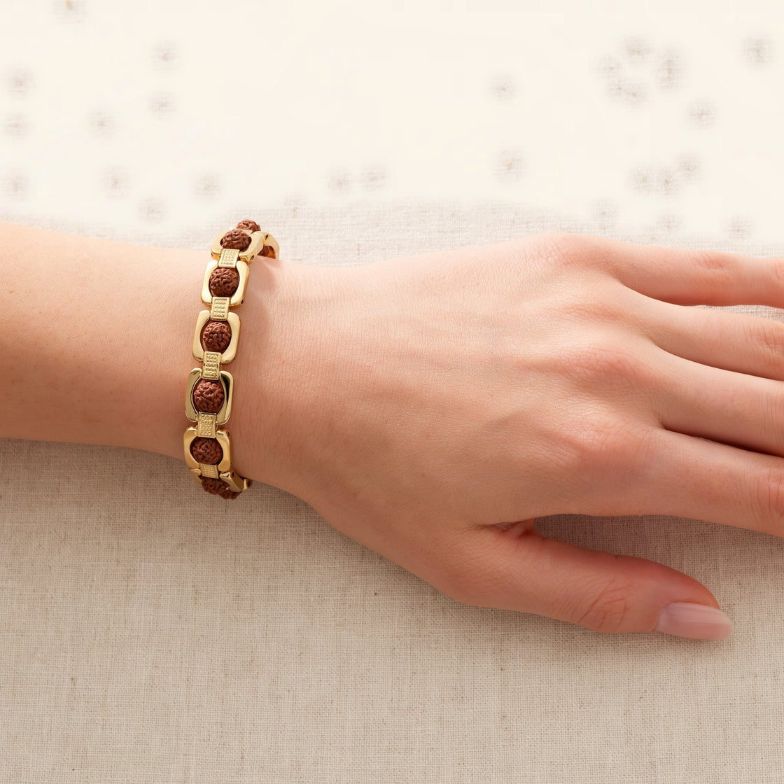 Close-up of a woman's wrist wearing a gold plated link bracelet with Rudraksha beads on cream cloth
