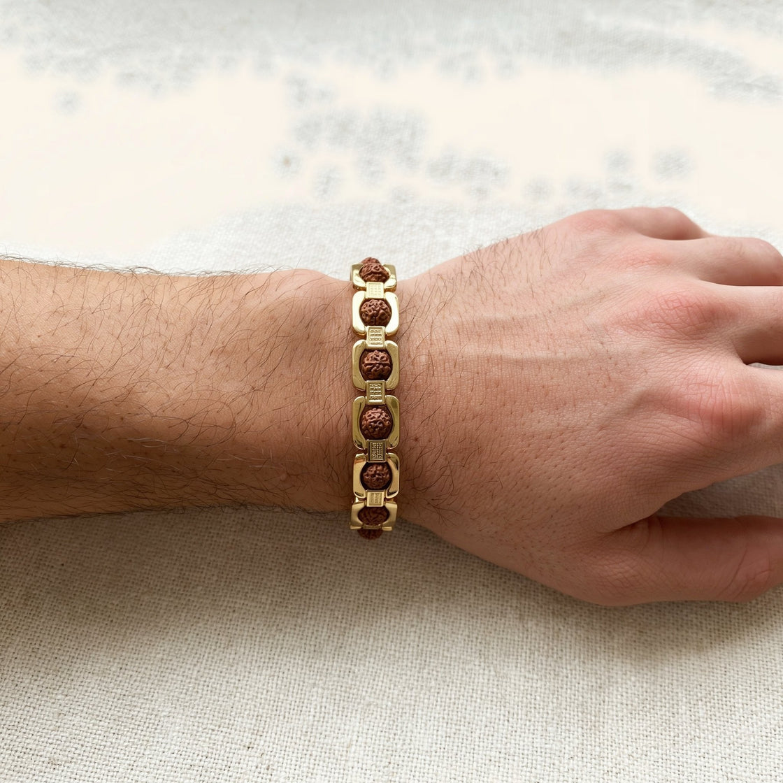 Close-up of a man's wrist wearing a gold plated link bracelet with Rudraksha beads on cream cloth