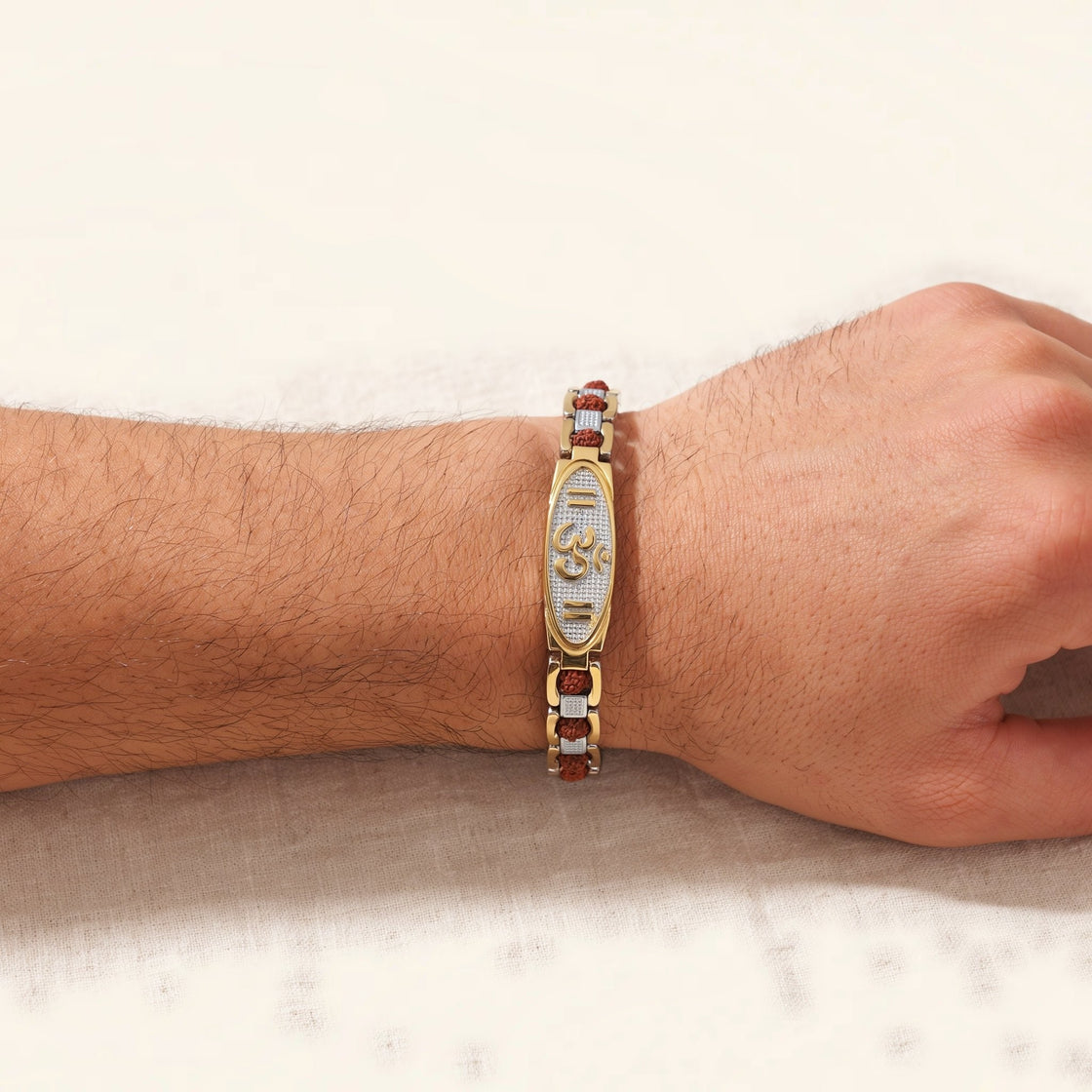 Man's wrist wearing an Om rudraksha bracelet with a gold and silver plate on cream cloth