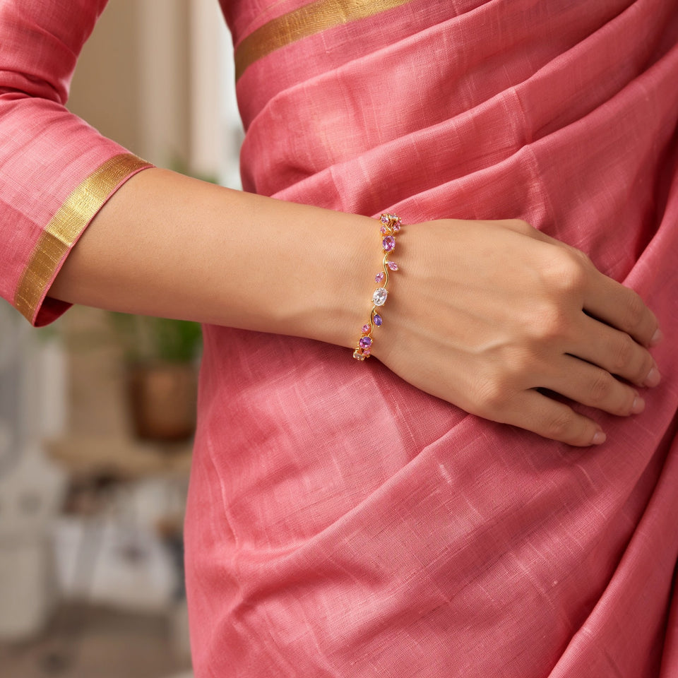 A woman's wrist in a pink saree sleeve with a gold border, wearing the pink and purple tulip bracelet