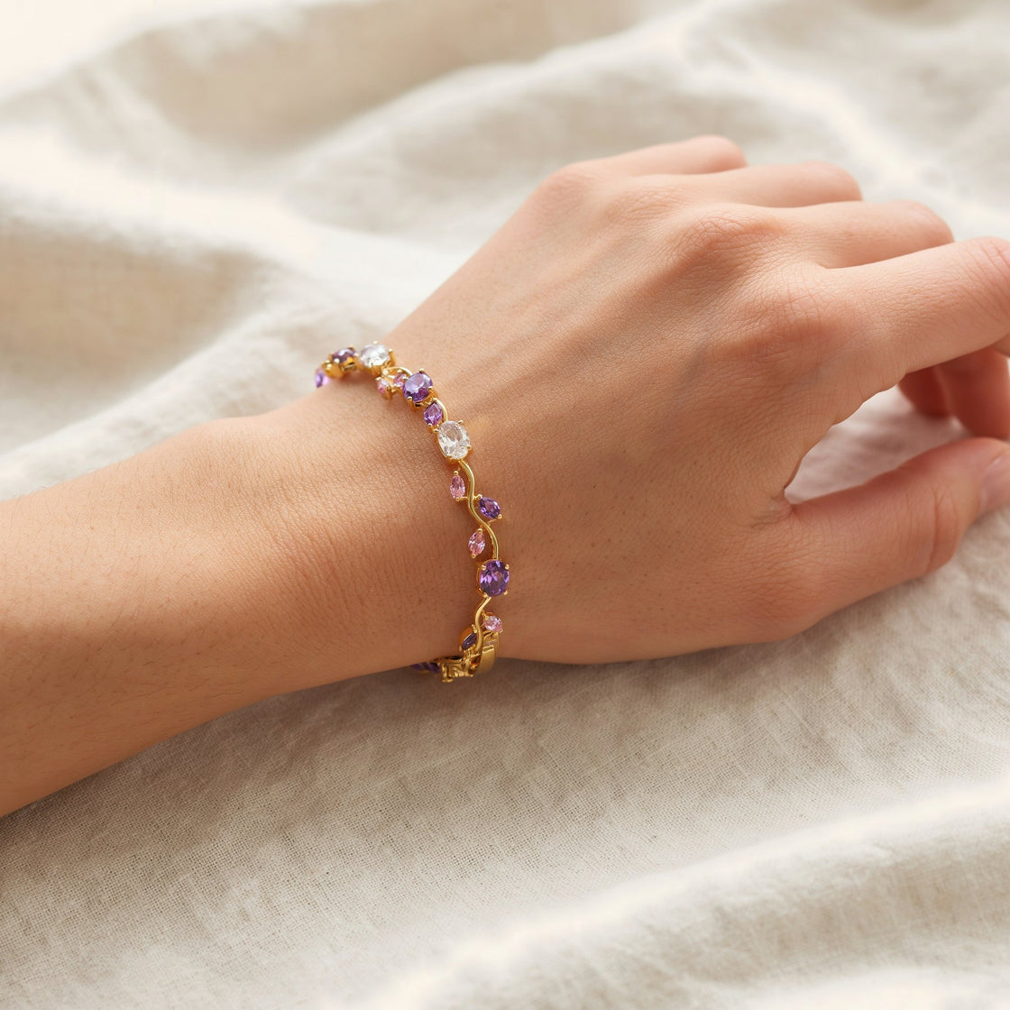 A woman's wrist resting on cream linen, wearing the pink and purple tulip bracelet