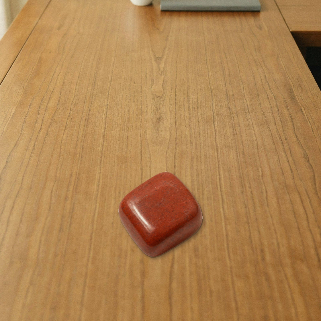red jasper tumble placed on a wooden desk