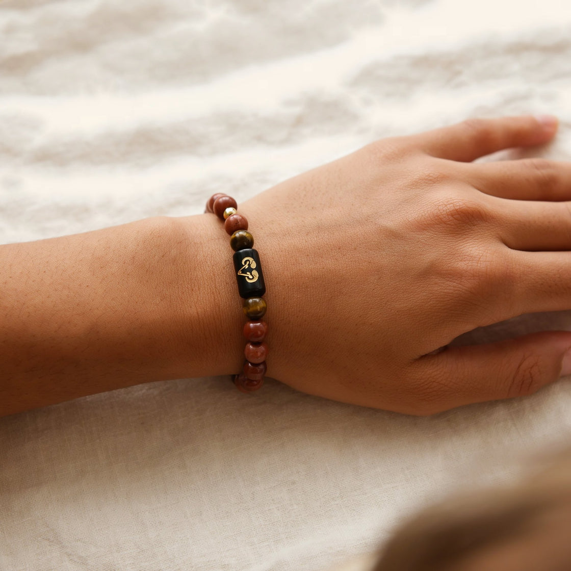 Woman's wrist wearing an Aries zodiac stone bracelet on cream linen