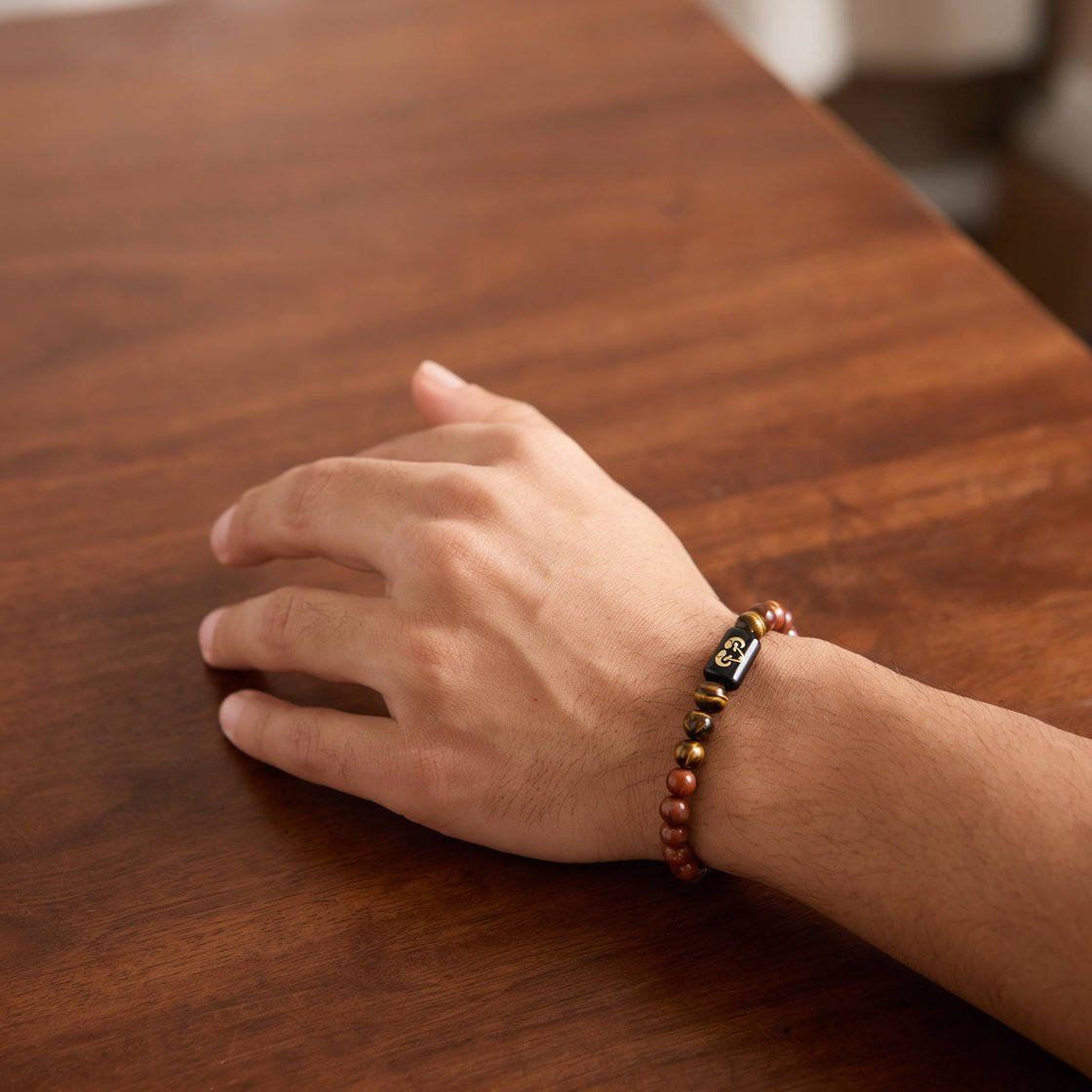 Man's wrist wearing an Aries zodiac stone bracelet on a wooden table
