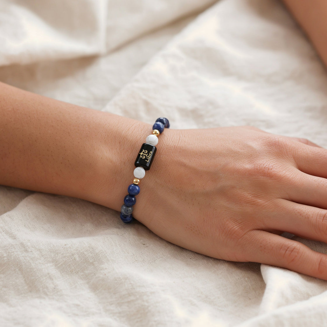 Woman's wrist wearing a Libra zodiac stone bracelet on cream linen