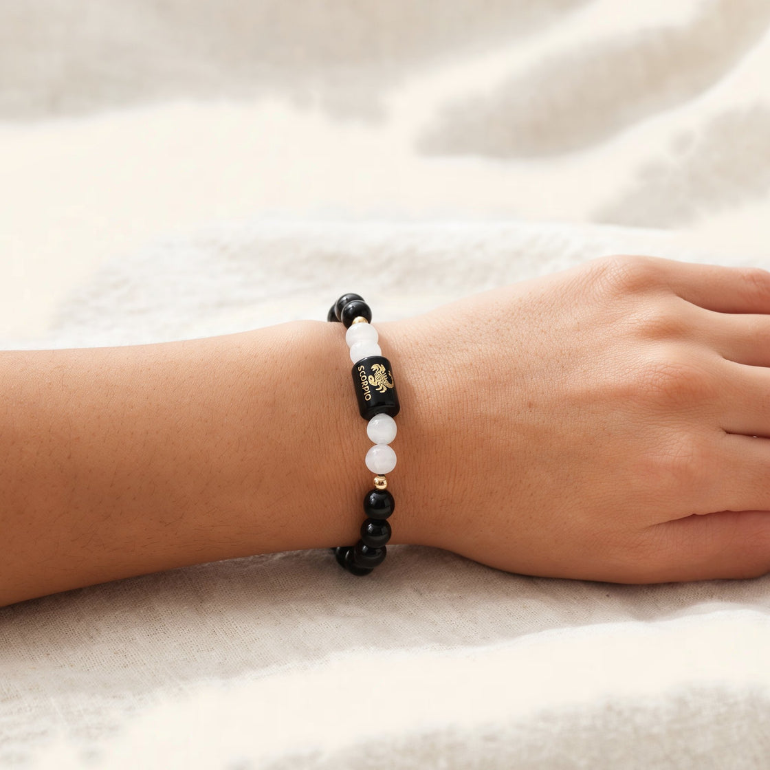 Woman's wrist wearing a Scorpio zodiac stone bracelet on cream linen