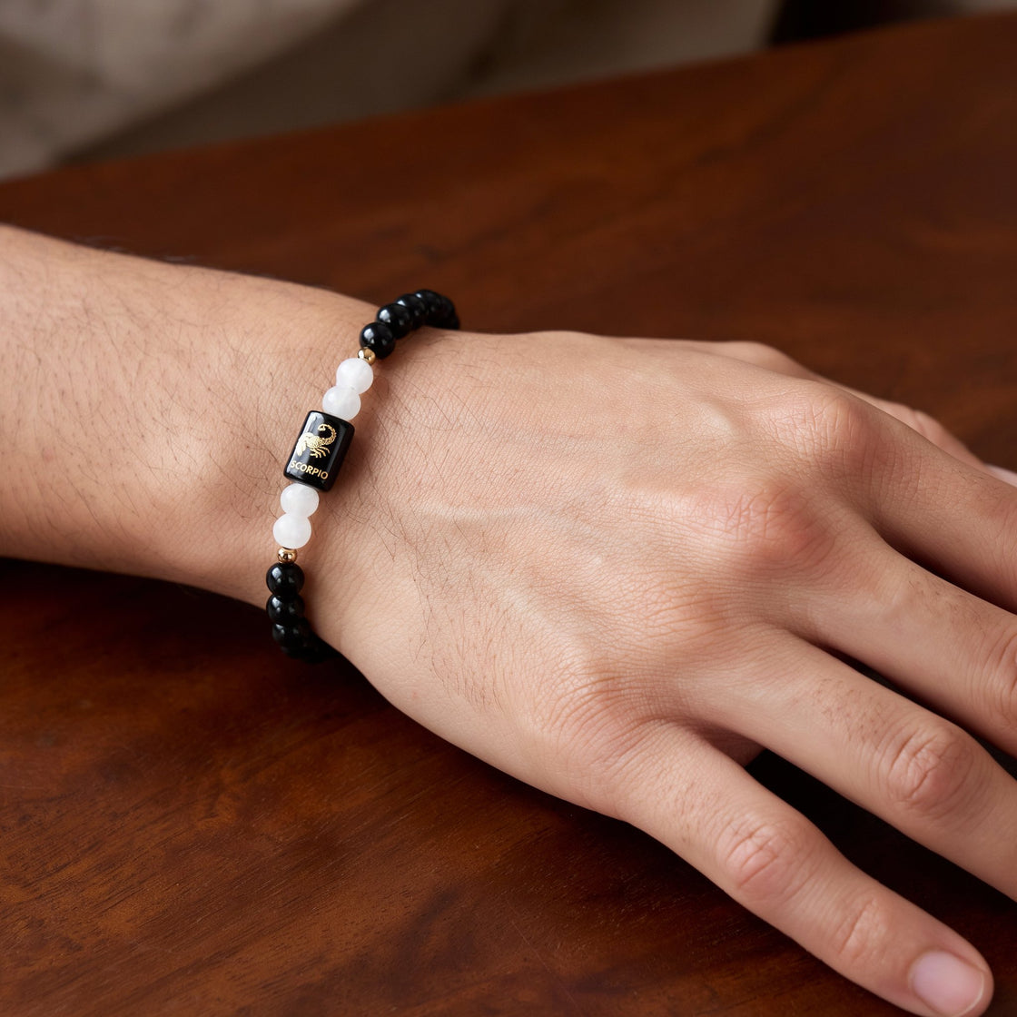 Man's wrist wearing a Scorpio zodiac stone bracelet on a wooden table