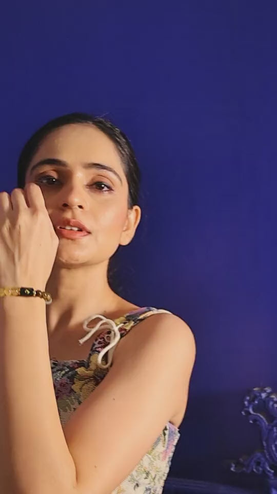 Woman in a floral top resting her chin on her hand, gold-and-black bracelet on the wrist
