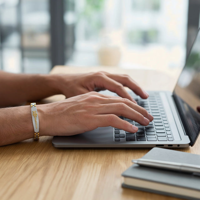 Man's wrist with a dual tone Trishul bracelet while typing on a laptop